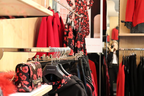 Modehaus-Gruber Kleiderstange mit roten und schwarzen Kleidern mit Blumenmuster, Spiegel und Regal im Hintergrund, Store-Einblick im Geschäft