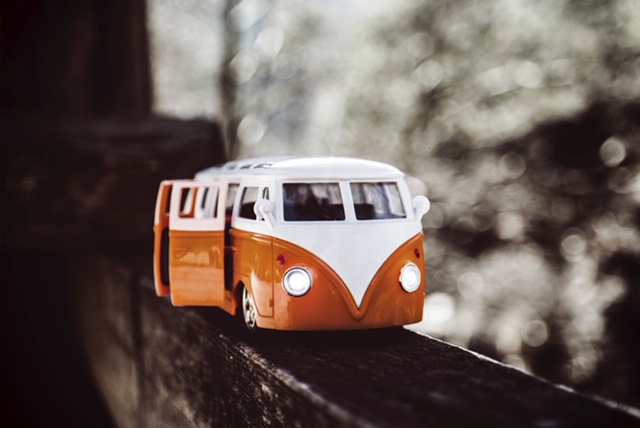 Miniature camper van in orange and white color, VW bus shape, small toy car on the edge of a tree, realistic details