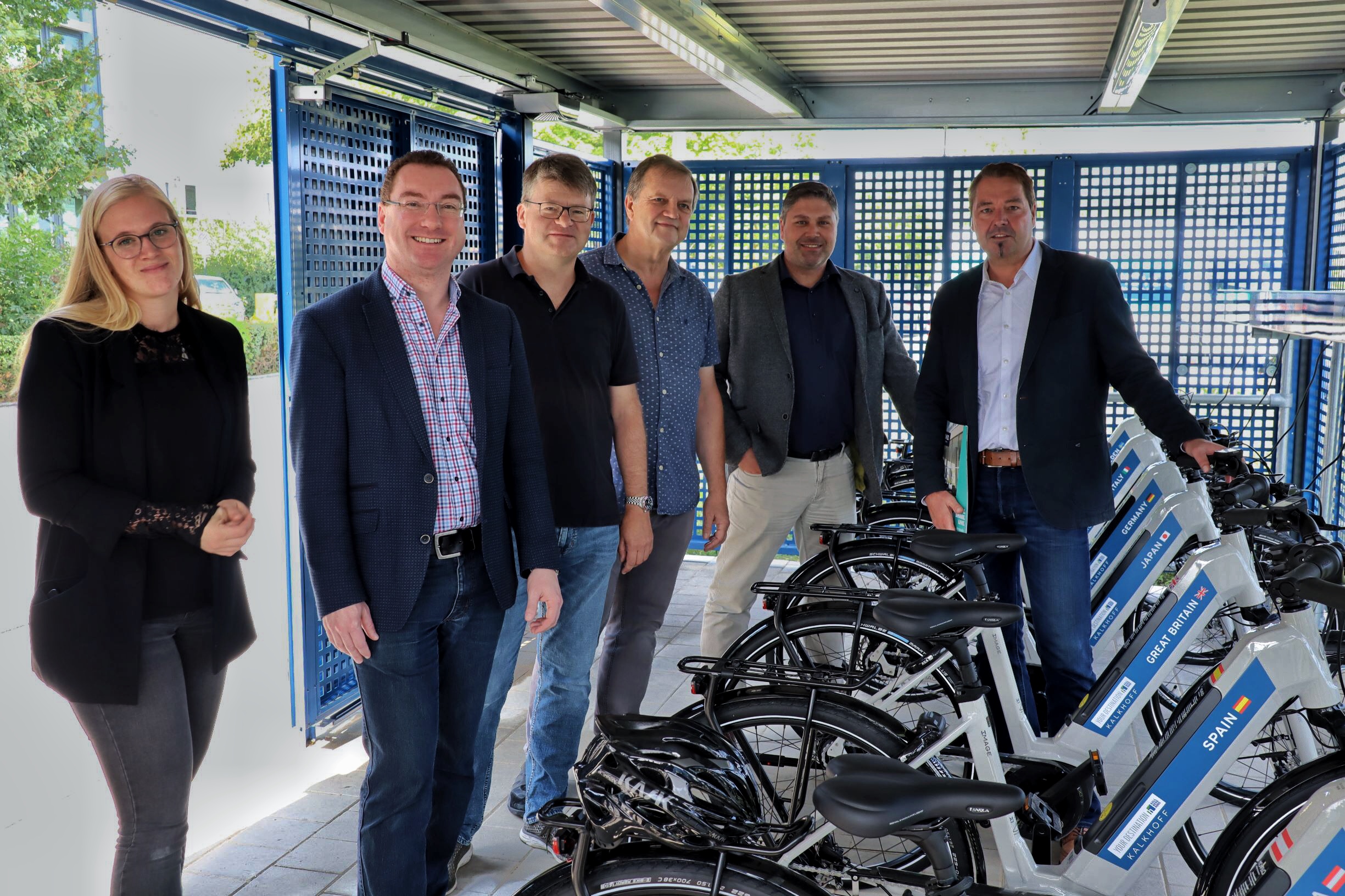 Group of people standing next to e-bikes at the Hallbergmoos site, bicycles in white with blue holder; public area of the MABP.