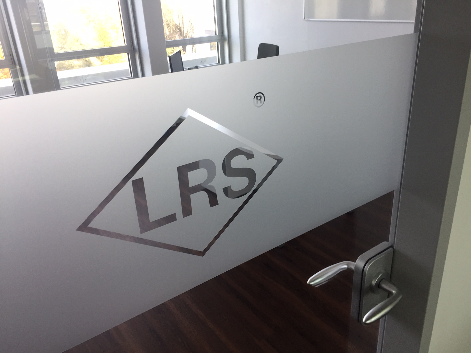 Glas Tür mit dem LRS Logo, die einen Besprechungsraum in einem modernen Bürogebäude zeigt.