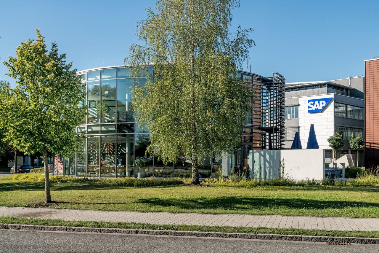 Glasfront eines modernen Bürogebäudes in Hallbergmoos, Fotograf Manfred Zentsch, umgeben von grünen Bäumen, SAP-Logo sichtbar, klare taghelle Szenerie