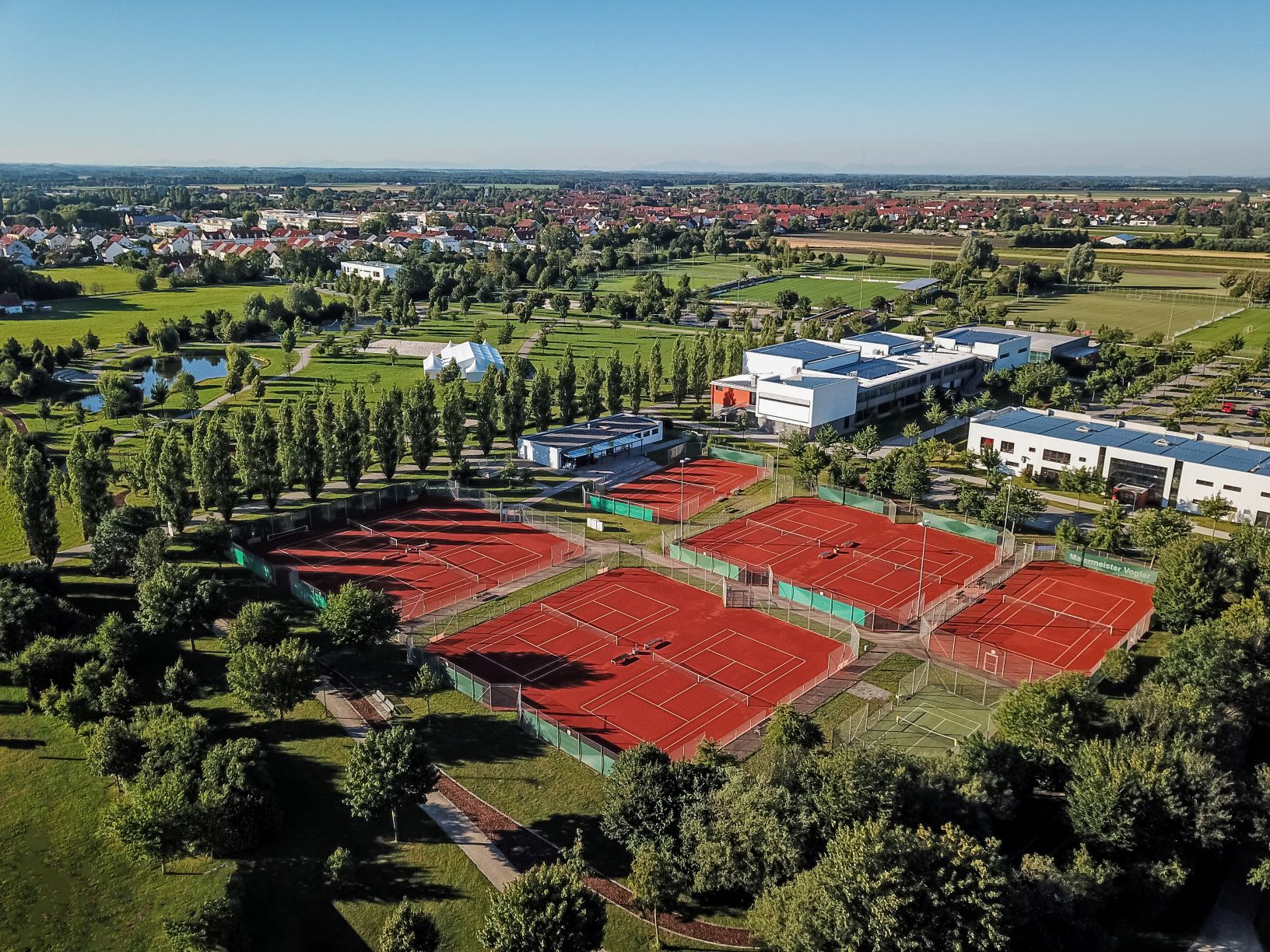 Luftaufnahme der roten Tennisplätze im MABP Gelände Hallbergmoos, umgeben von Grünflächen, Bäumen und modernen Gebäuden; Vogelperspektive, Fotograf Manfred Zentsch