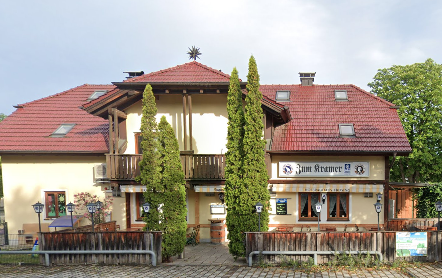 Gaststätte zum Kramer mit zwei hohen Zypressen und einem roten Dach in einer ruhigen Umgebung.