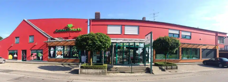 Rote Fassade des Goldachmarkts mit großen Fenstern und Bäumen im Vordergrund.