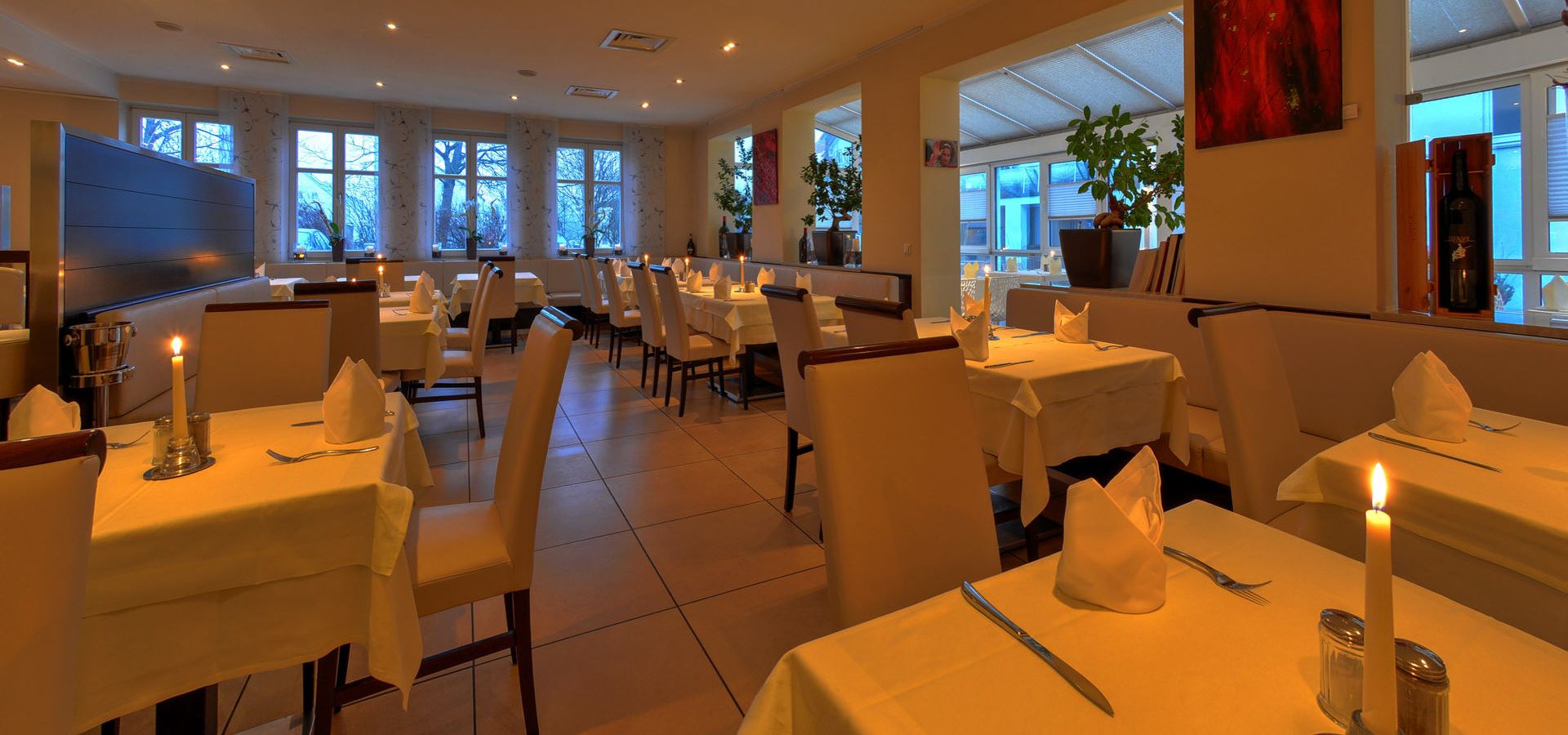 Innenansicht eines Restaurants mit Tischen, Stühlen und Kerzenlicht.