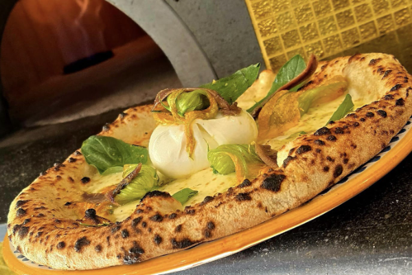 Pizza OroDiNapoli mit frischem Mozzarella, Spinat und Oliven auf einem Teller.