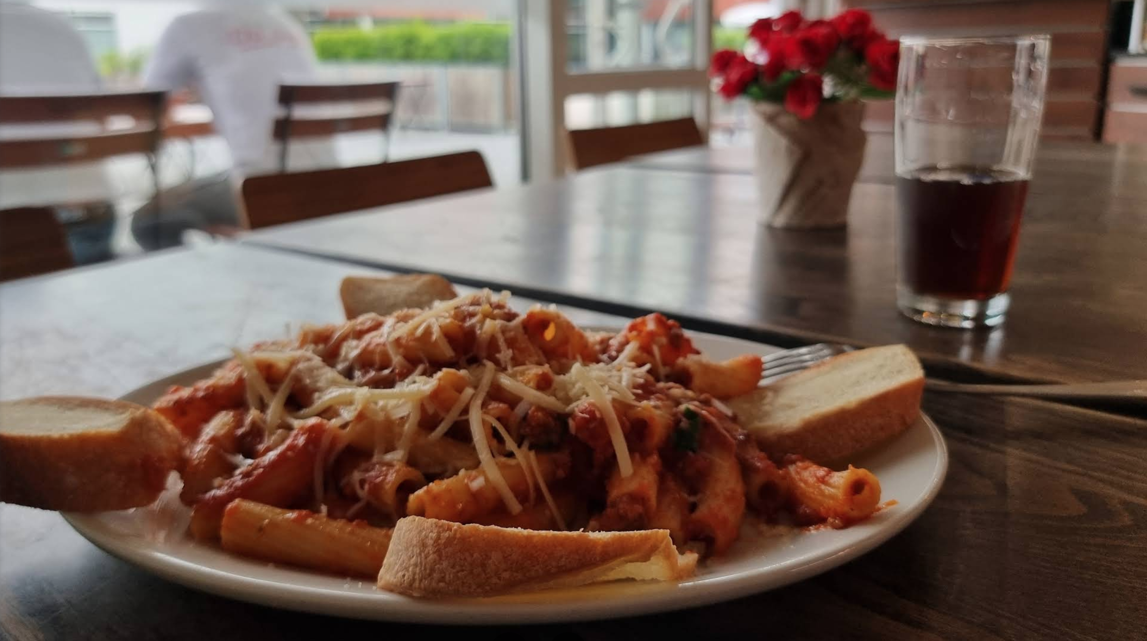 Teller mit Pasta, Tomatensauce, Käse und Brot auf einem Tisch in einem Restaurant.