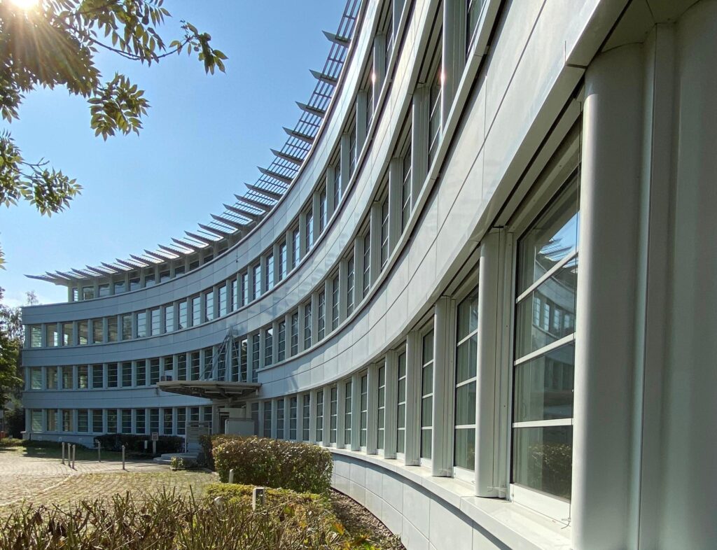 Ludwigstrasse45 Frontansicht eines modernen, grauen Bürogebäudes mit kurvenförmiger Fassade und vielen Fenstern am Munich Airport Business Park (MABP), München