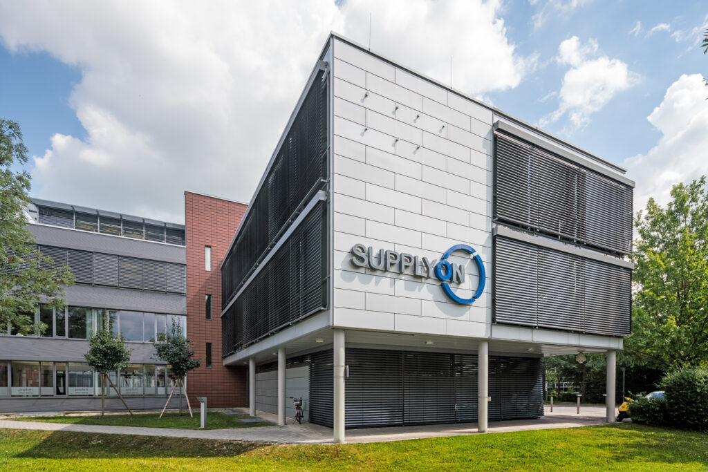 Moderne Gebäude mit dem Logo von SUPPLYON an der Fassade, umgeben von Bäumen und Rasenflächen.
