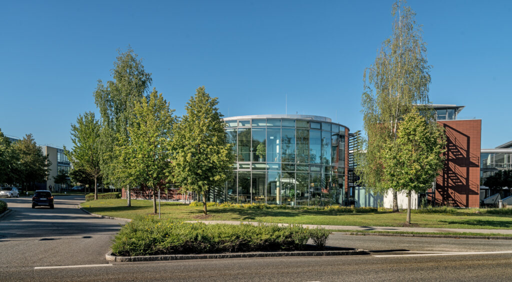 Moderne Architektur eines Bürogebäudes mit großen Glasfenstern und umliegenden Bäumen im Münchener Flughafen Business Park.