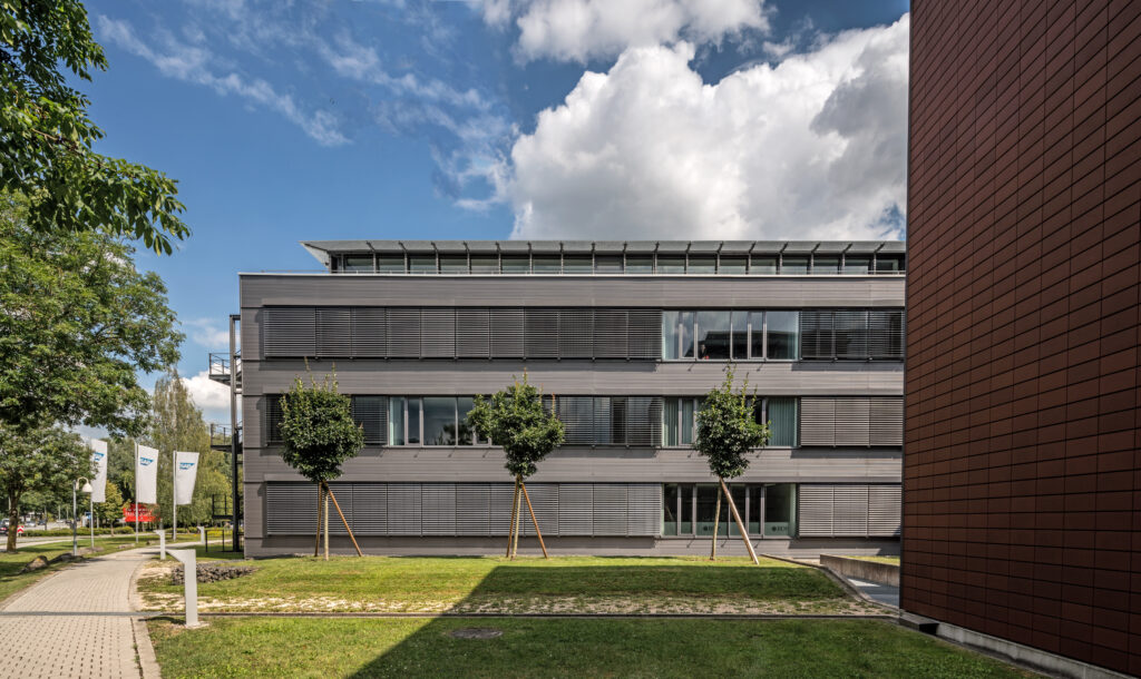 Moderne Gebäude mit horizontalen Fensterläden und Bäumen im Vordergrund im Münchener Flughafen Business Park.