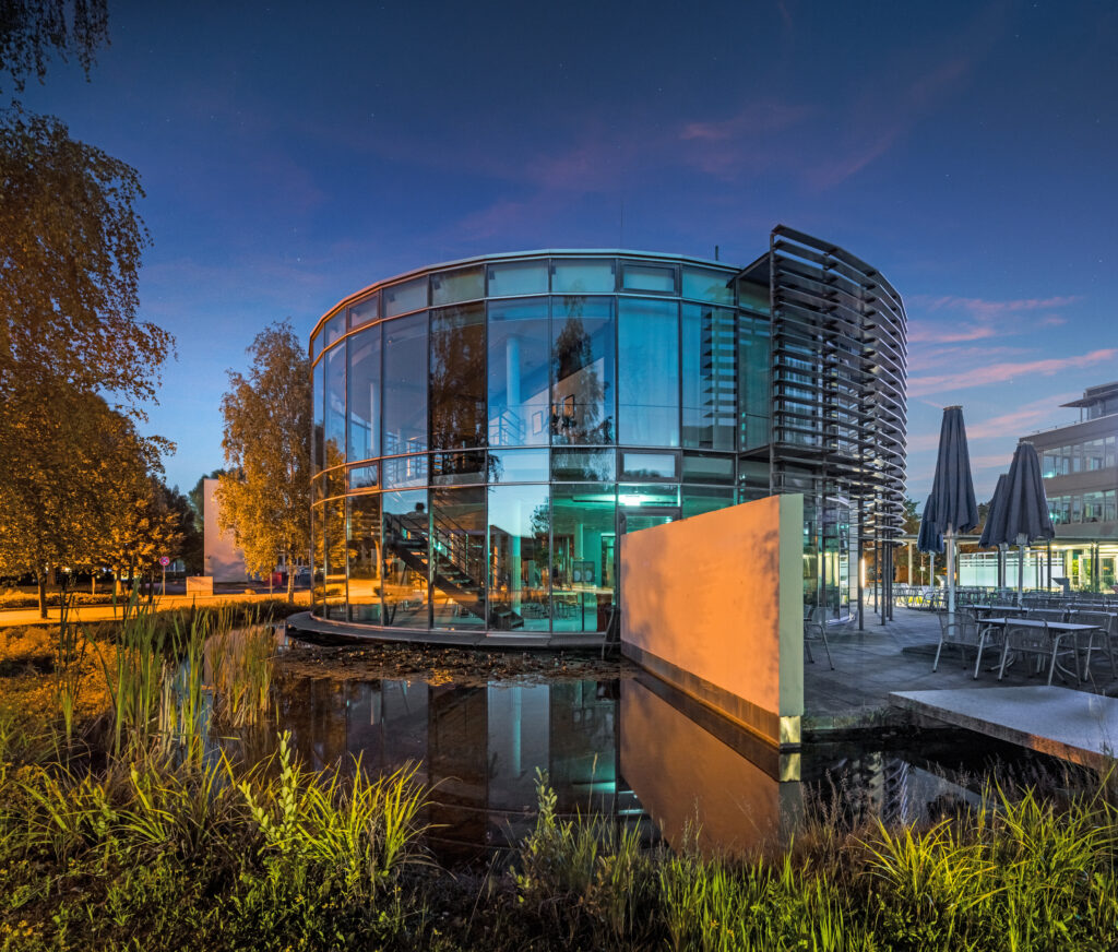Moderne Glasarchitektur eines Gebäudes mit runder Form und reflektierenden Fenstern im Münchener Flughafen Business Park.