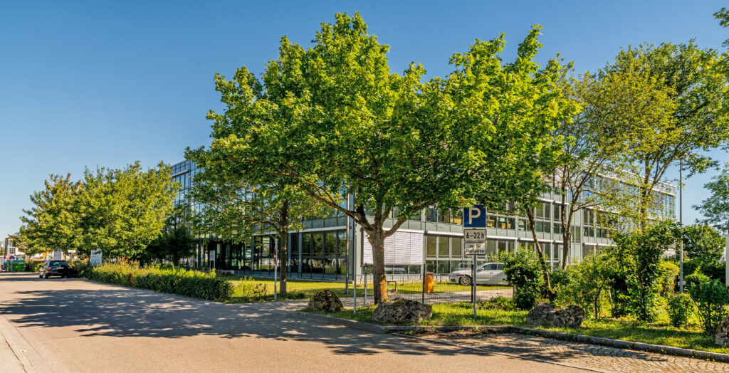 Moderne Bürogebäude mit großen Fenstern und umliegenden Bäumen im Münchener Flughafen Business Park.