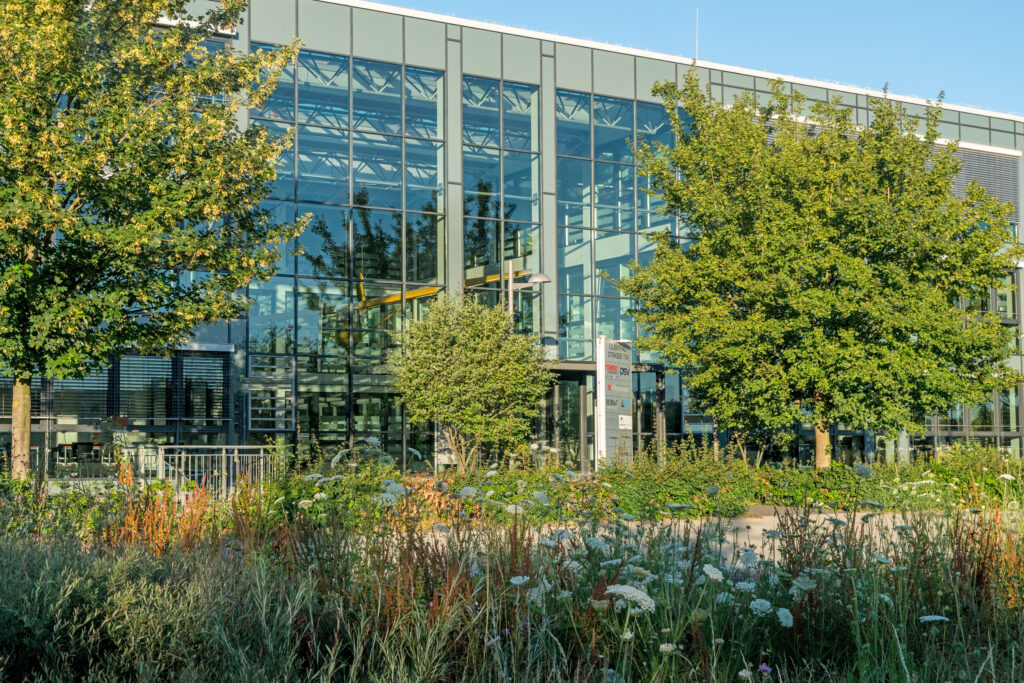 Moderne Architektur eines Bürogebäudes mit großen Glasfenstern und umliegender Vegetation.