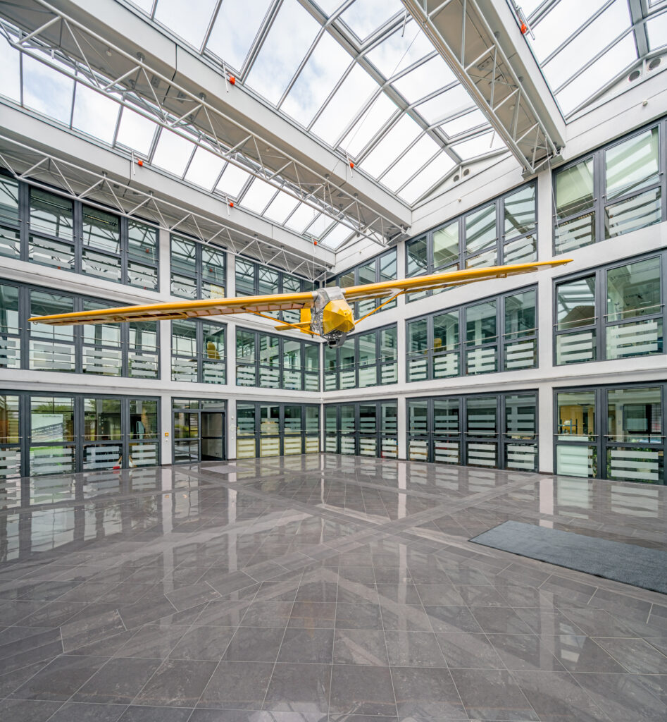 Gelbes Flugzeugmodell, das in einem modernen Innenraum mit großen Fenstern und glänzendem Boden schwebt.