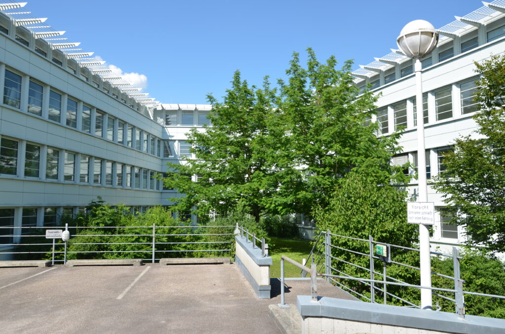 Blick auf einen modernen Bürokomplex mit großen Fenstern und einem Baum im Vordergrund.