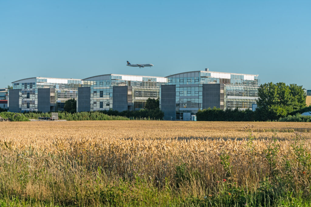 Moderne Bürogebäude des MABP mit einem Flugzeug, das über das Gelände fliegt.