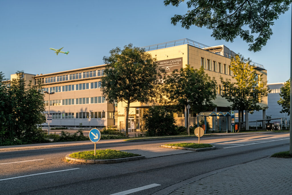 Gebäude des Lindbergh Centers in der Nähe des Münchener Flughafens mit einem Flugzeug im Hintergrund.