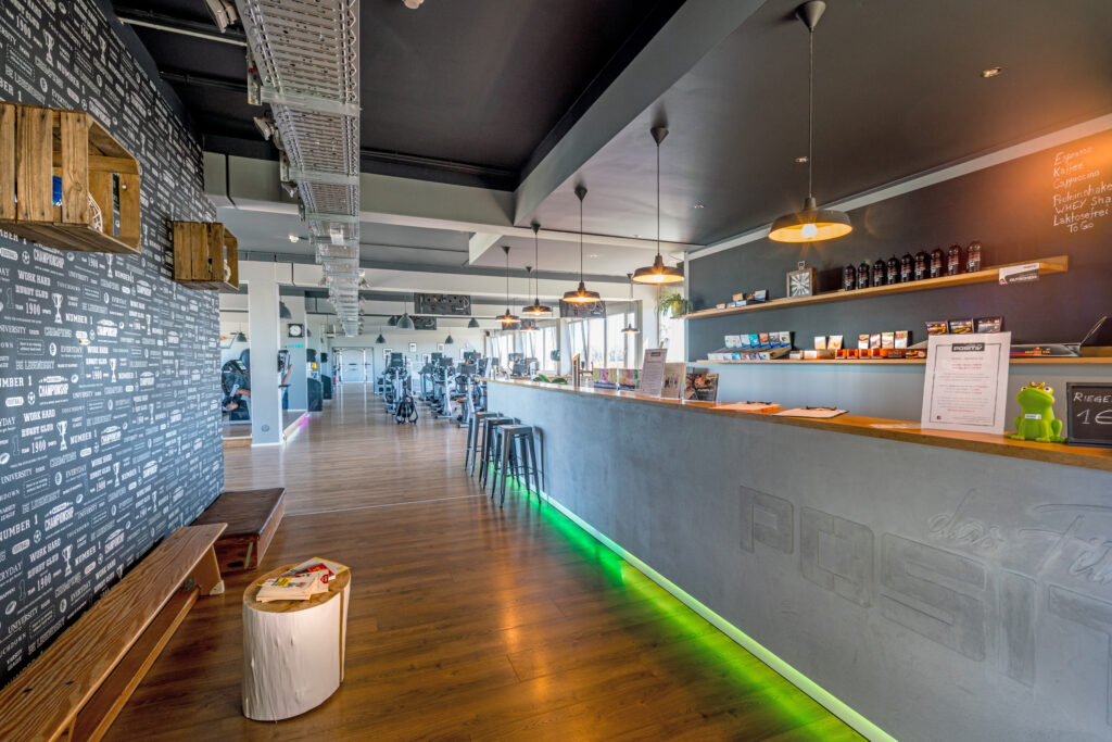 Moderne Empfangstheke in einem Fitnessstudio mit Holzregalen und Beleuchtung.