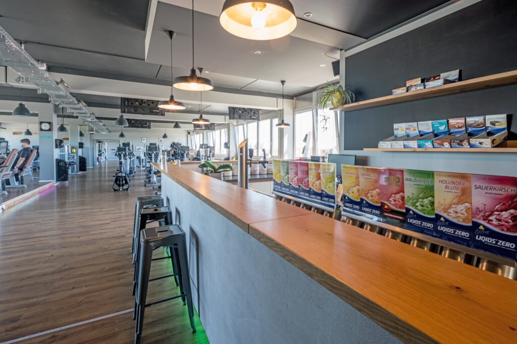 Moderne Fitnessstudio-Innenansicht mit einem langen Holztheke und verschiedenen Getränken in bunten Verpackungen.