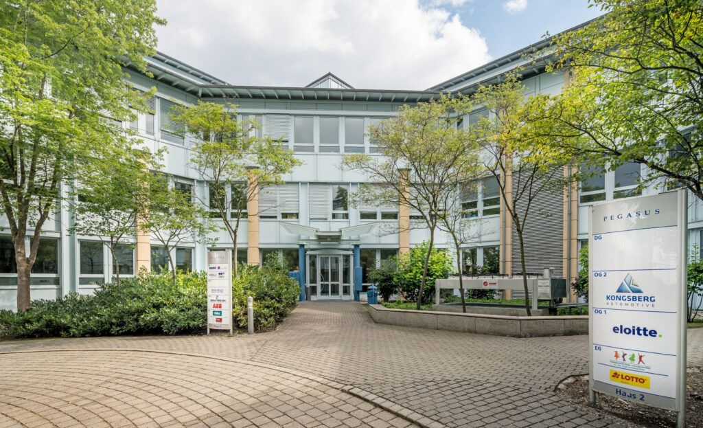 Eingang zum PEGASUS-Gebäude mit Schildern von KONGSBERG und eloiitte in einem Bürokomplex.