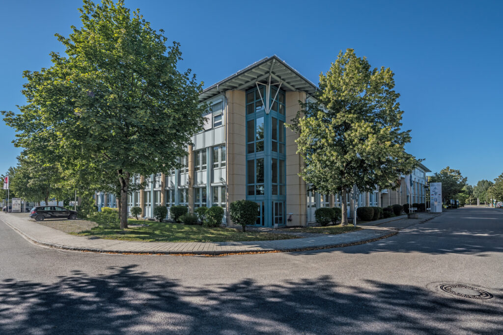 Moderne Bürogebäude mit großen Fenstern und Bäumen im Vordergrund.