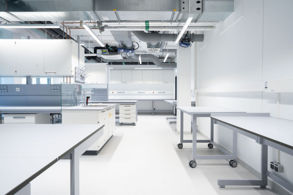 Moderne Laborumgebung mit mehreren Arbeitstischen und einem Labortisch im Hintergrund.