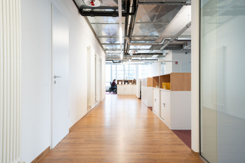 Büroflur mit Holzfußboden und modernen Trennwänden in einem Geschäftshaus.