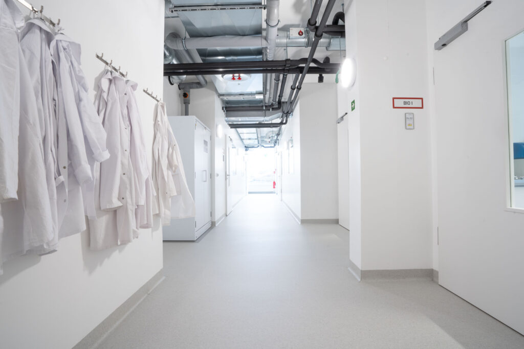 Helle Korridoransicht mit weißen Laborkitteln, die an einem Haken hängen.
