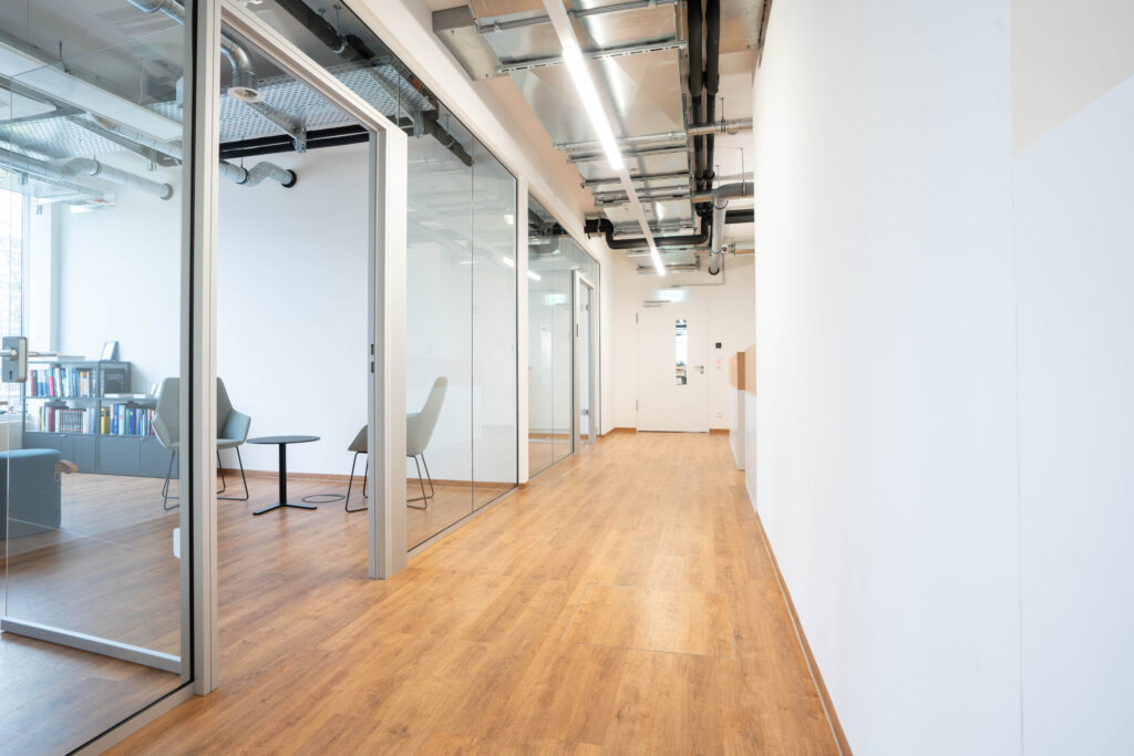Büroflur mit Glaswänden und Holzfußboden im MABP-Gebäude.
