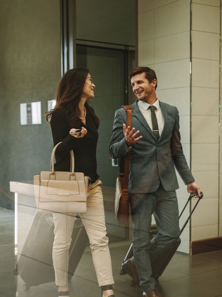 Ein Mann in einem Anzug und eine Frau mit einer Handtasche gehen mit Gepäck in einem modernen Gebäude.